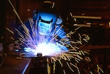 A person in black protective gear welds, as sparks fly.