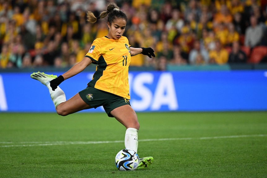 A woman in a yellow football shirt looks to kick a ball very hard.