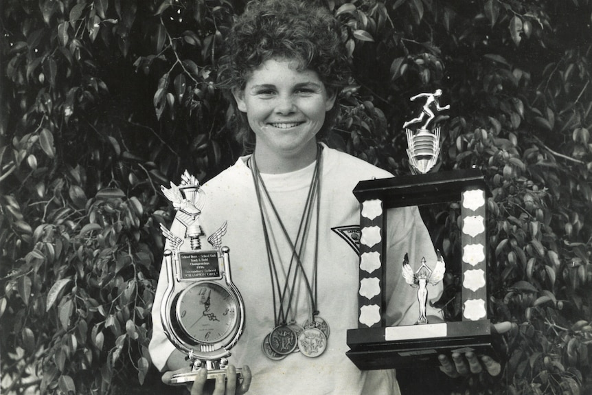Young teenage girl holding various trophies and wearing medals.