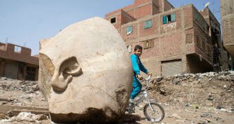 A boy rides past a recently discovered statue in a Cairo slum.