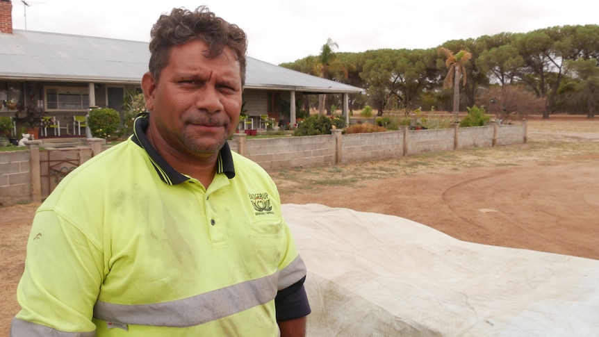 an aboriginal ranger in high-vis stands before a house