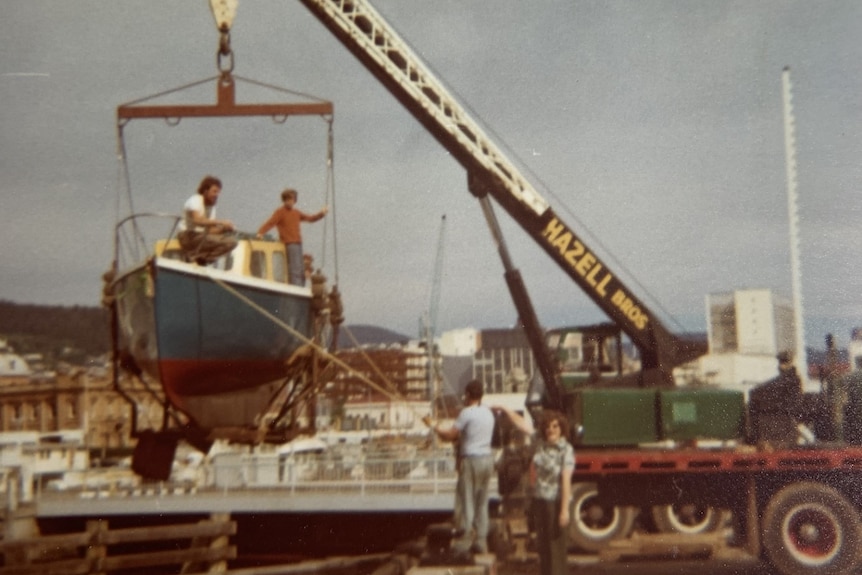 an old photo of a small boat being launched into the water with a crane