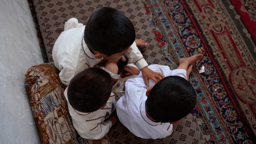 Three young children sit on a rug. The photo is taken from above them and their faces are hidden.