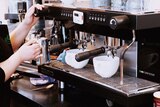 Barista warms milk at industrial coffee machine.