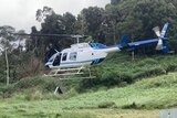 A helicopter lands in a paddock with gas bottles in the foreground.