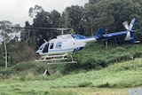 A helicopter lands in a paddock with gas bottles in the foreground.