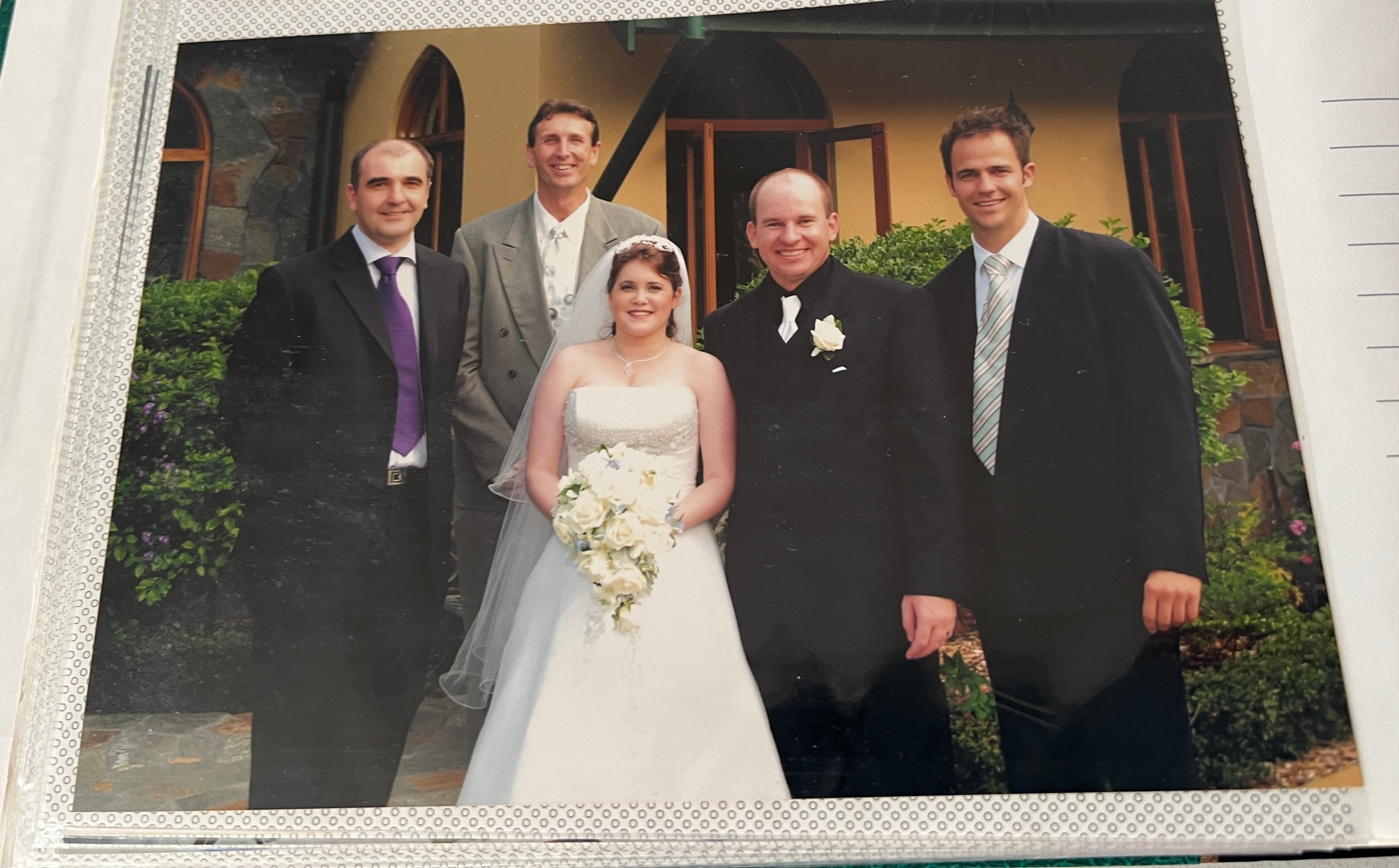 A woman in a wedding dress and four men in suits smiling at the camera 