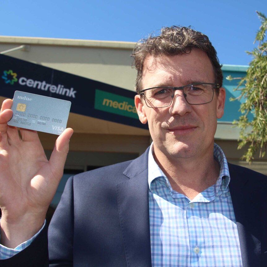Human Services Minister Alan Tudge holding a cashless welfare card while standing outside Centrelink in Kalgoorlie.