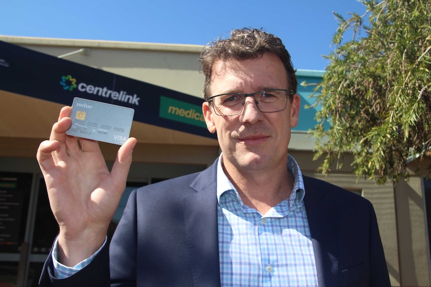 Human Services Minister Alan Tudge holding a cashless welfare card while standing outside Centrelink in Kalgoorlie.