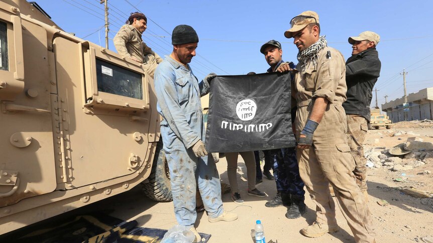 Iraqi soldiers pose with the Islamic State flag along a street in the Intisar district of eastern Mosul, Iraq.