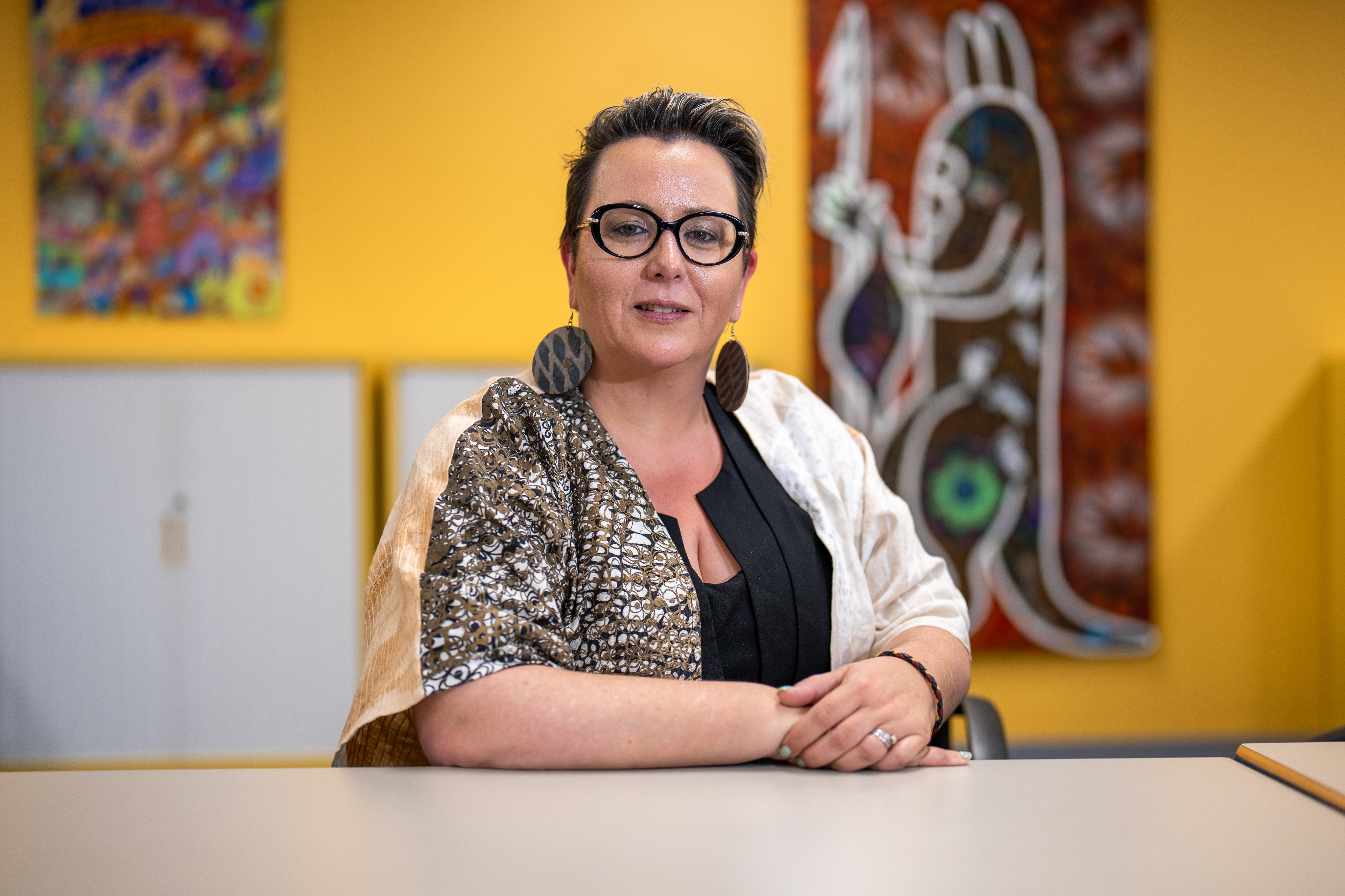 A woman with her hands folded in front of her against a blurred background.