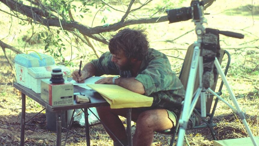 Les Hiddins writes field notes on a fold-up table in the bush.