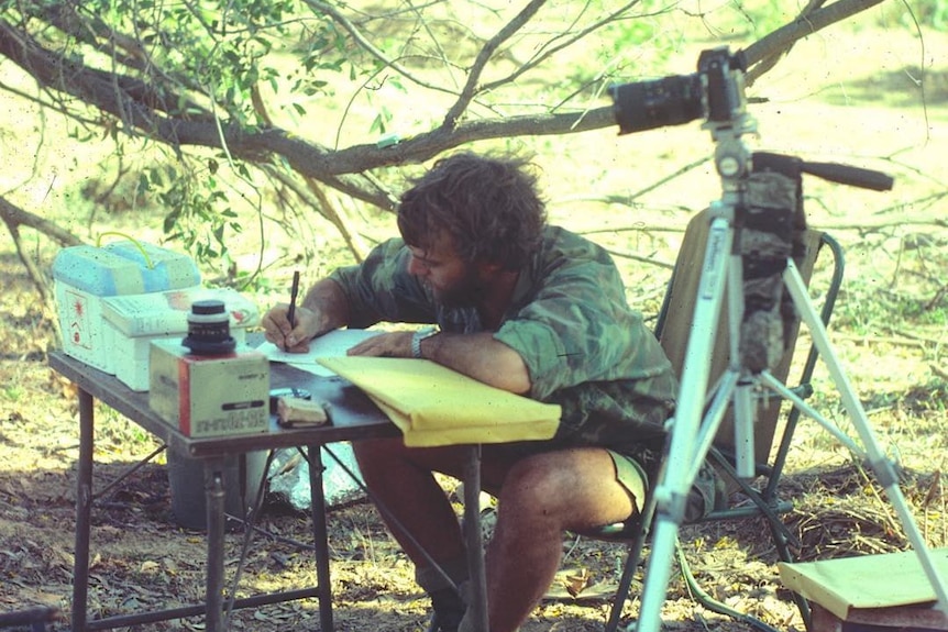Les Hiddins writes field notes on a fold-up table in the bush.