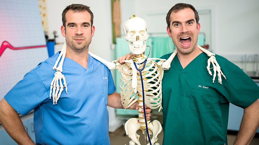 Two men dressed in scrubs pose for photo with skeleton