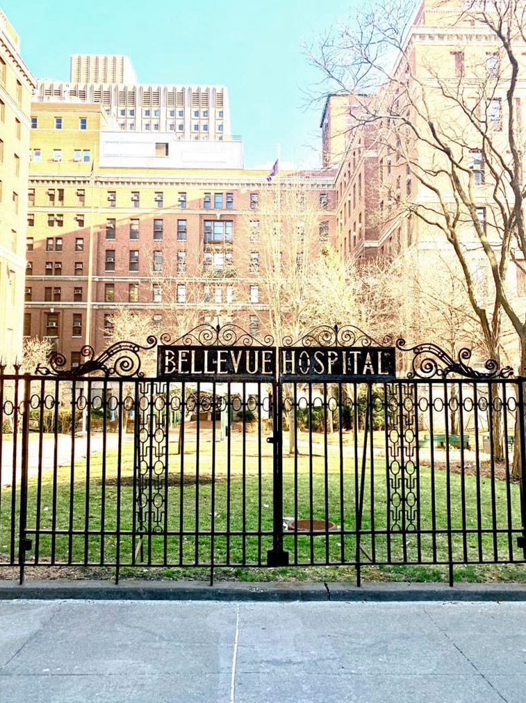 A sign says 'Bellevue Hospital' on gates outside a large building.