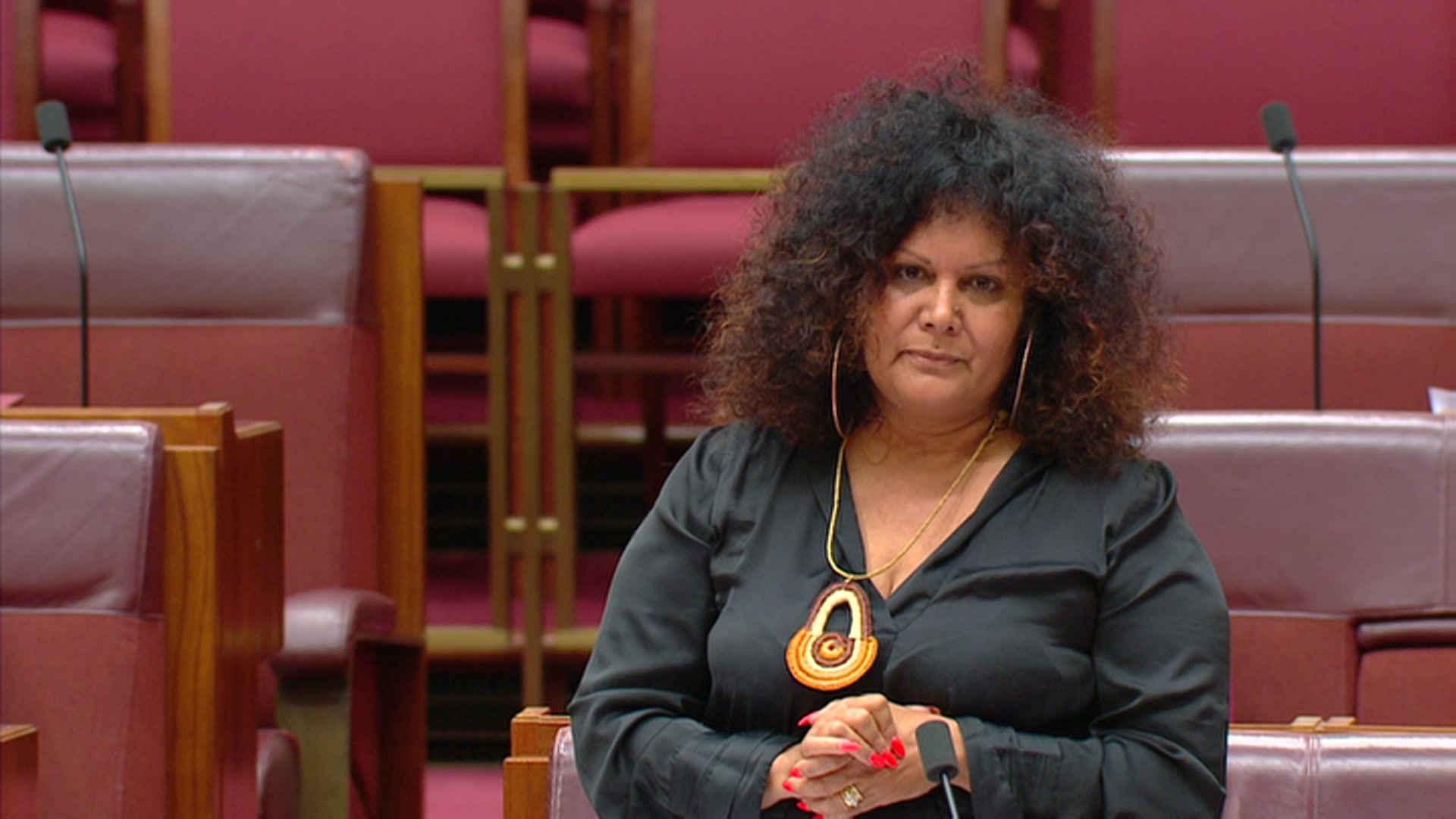 A woman looks at the camera, in a room with maroon furnishings.