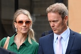 A man wearing a suit and a woman wearing a green dress and sunglasses