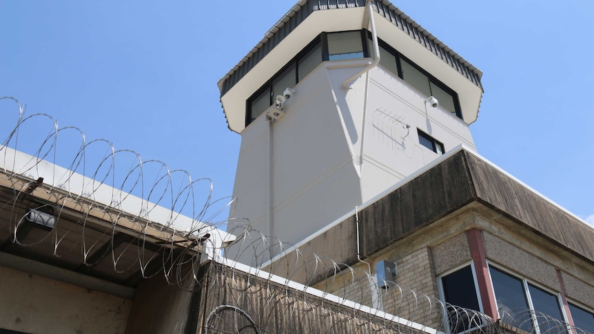 A watch tower looming above a large concrete fence topped with barbed wire surrounding Don Dale.