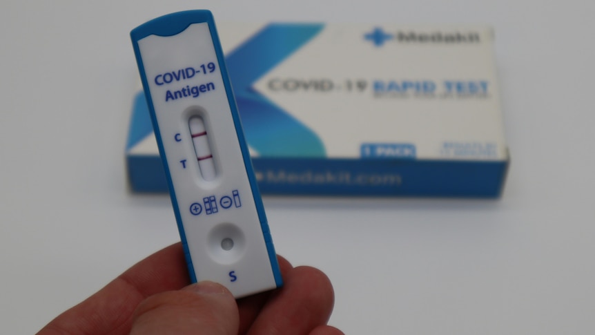 a positive covid test in someone's hand, with the box behind it