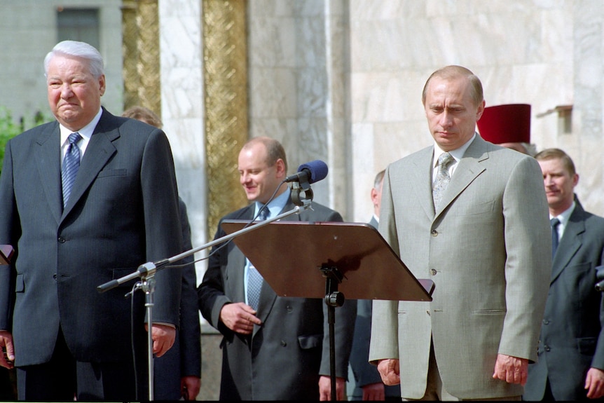 Two white men in suits stand on a stage.