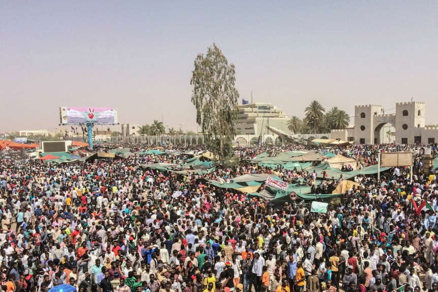 From a balcony, you look down and see hoards of people gathered on a street as the sky turns to pale blue.