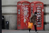 A woman in a face mask walks past a red telephone box.