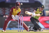 David Warner swings the bat on a cricket pitch with a wicketkeeper in red standing behind the stumps.