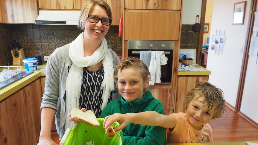 A mum and her two sons, aged 5 and 8, put fruit scraps in a small kitchen bin.
