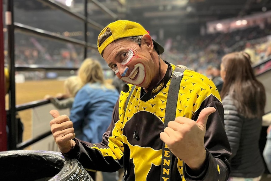 Man dressed in clown costume and makeup giving a thumbs up action with his hands. 