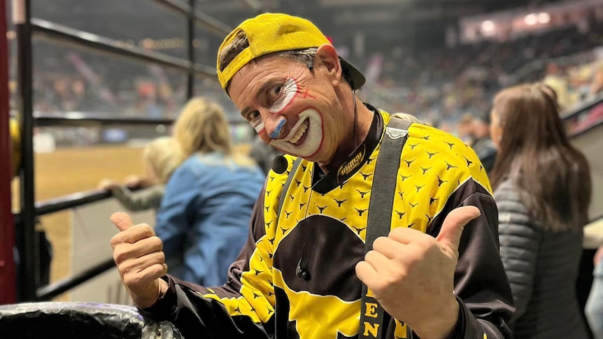 Man dressed in clown costume and makeup giving a thumbs up action with his hands. 