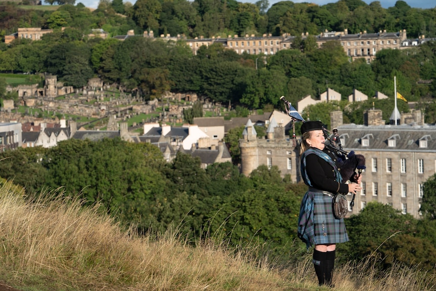 A bagpipe player stands on the cliff. 