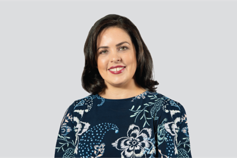 a woman with dark brown hair smiles at the camera. She is wearing a blue floral shirt.