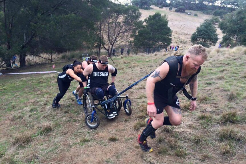 Man in wheelchair being dragged up a hill by group of friends