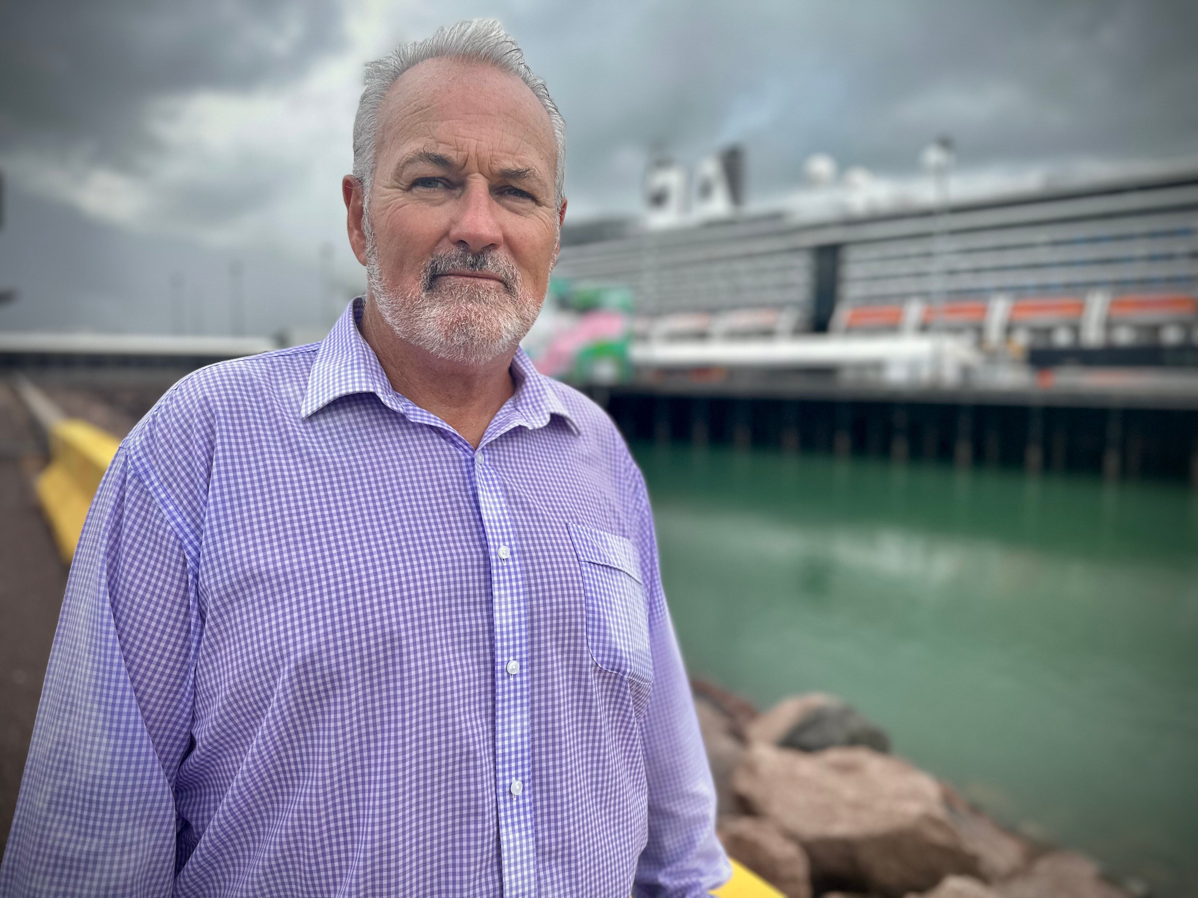 A man standing on a pier and looking serious, with a large ship in the background. 