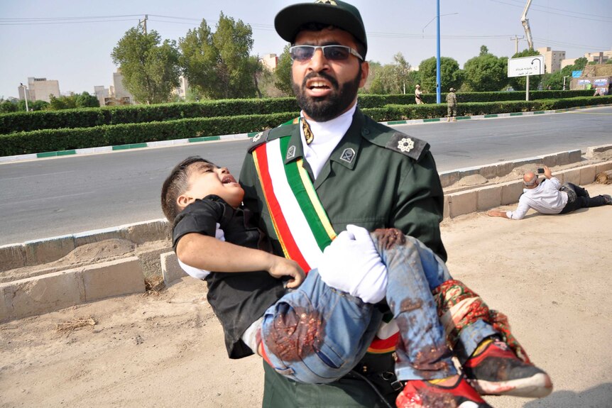 Man in uniform who looks anguished carries a crying young boy with blood on his jeans