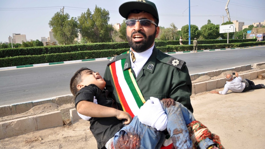 Man in uniform who looks anguished carries a crying young boy with blood on his jeans