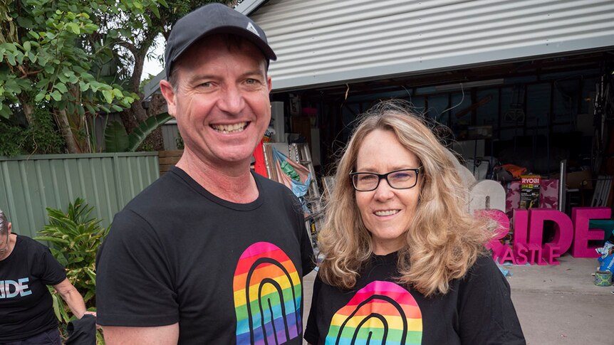A man and a woman both wearing Newcastle Pride shirts in a suburban back yard.