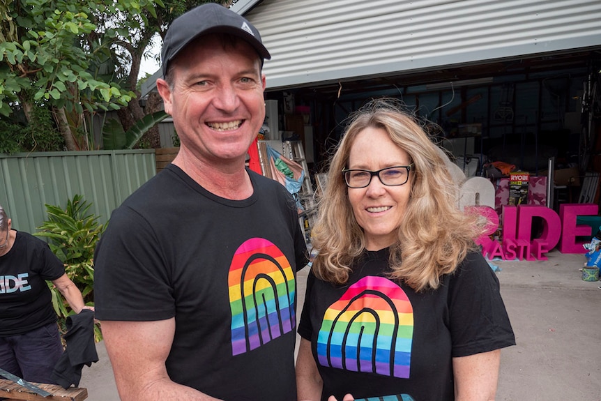 A man and a woman both wearing Newcastle Pride shirts in a suburban back yard.