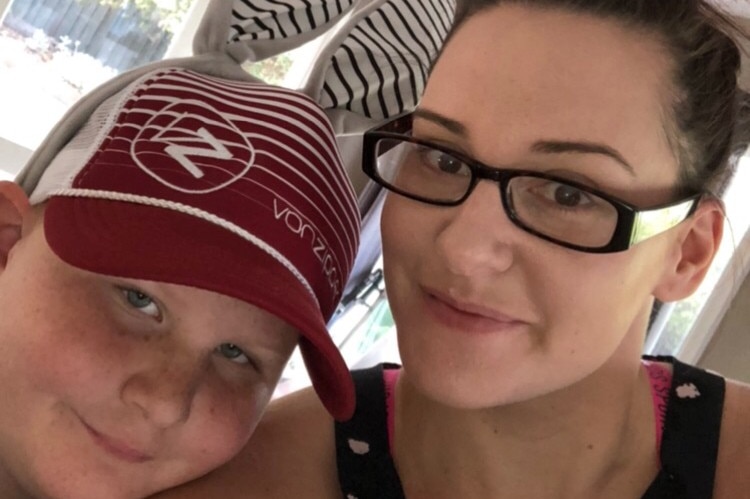 A selfie of a boy wearing a baseball cap and bunny ears with his mum.