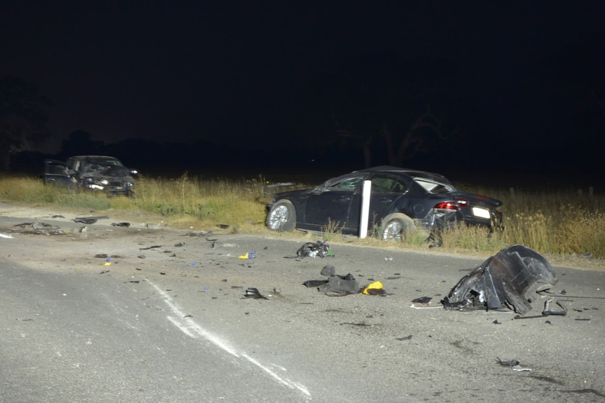 A badly damaged, dark-coloured sedan on the side of a road at night.
