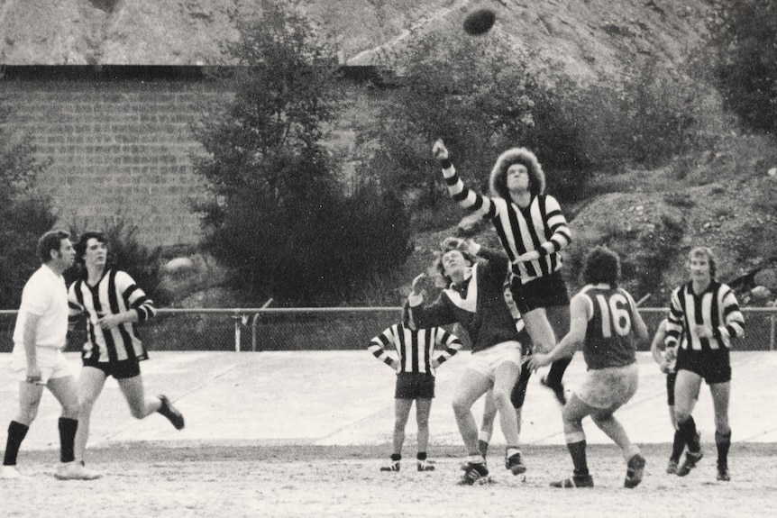 A ruckman with lots of frizzy hair leaps over the pack on the gravel oval