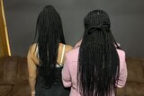 Two teenage girls with long, dark, braided hair. Their backs are to the lens.
