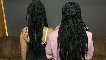 Two girls with backs to camera with long, braided black hair.