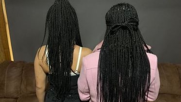 Two teenage girls with long, dark, braided hair. Their backs are to the lens.