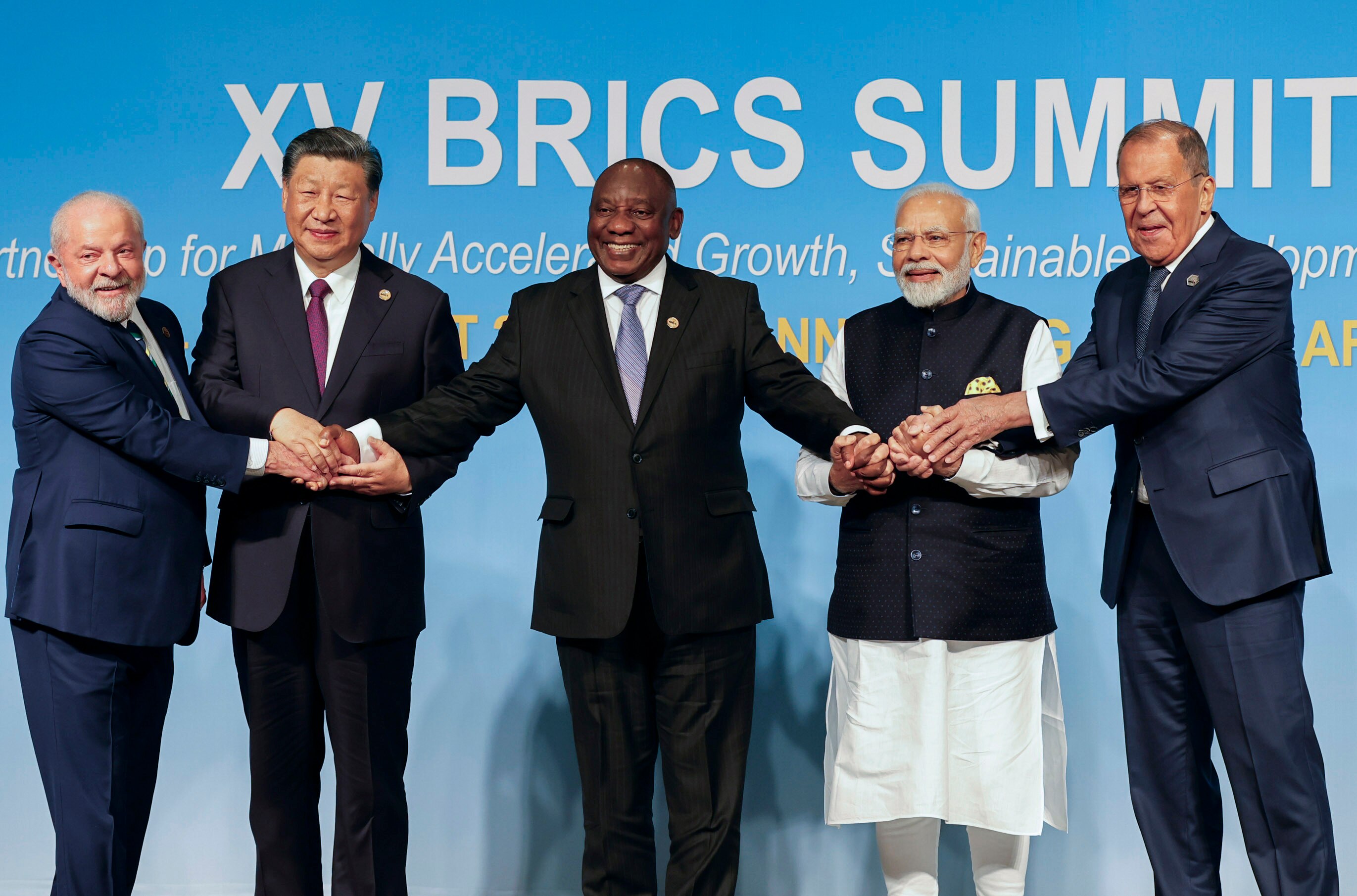 The leaders of Brazil, China, South Africa and India and Russia's foreign minister hold hands as they pose for a photo.