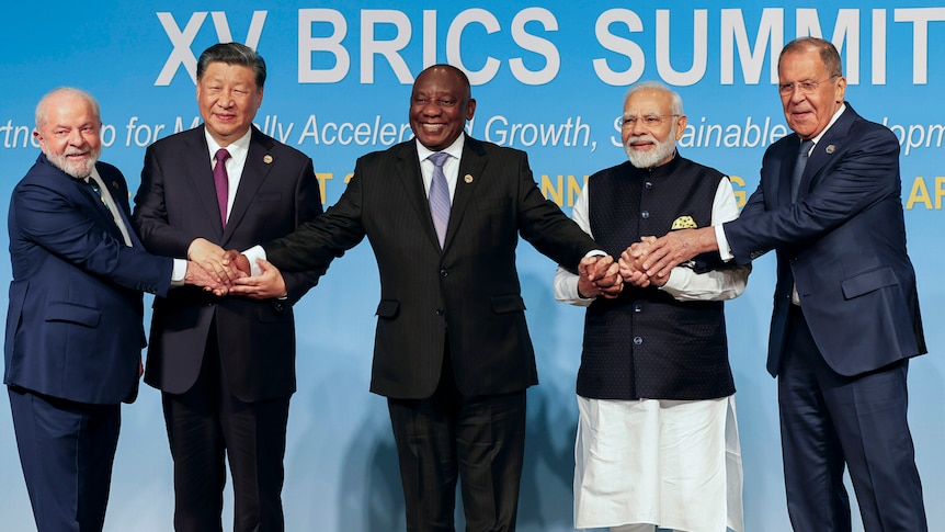 The leaders of Brazil, China, South Africa and India and Russia's foreign minister hold hands as they pose for a photo.