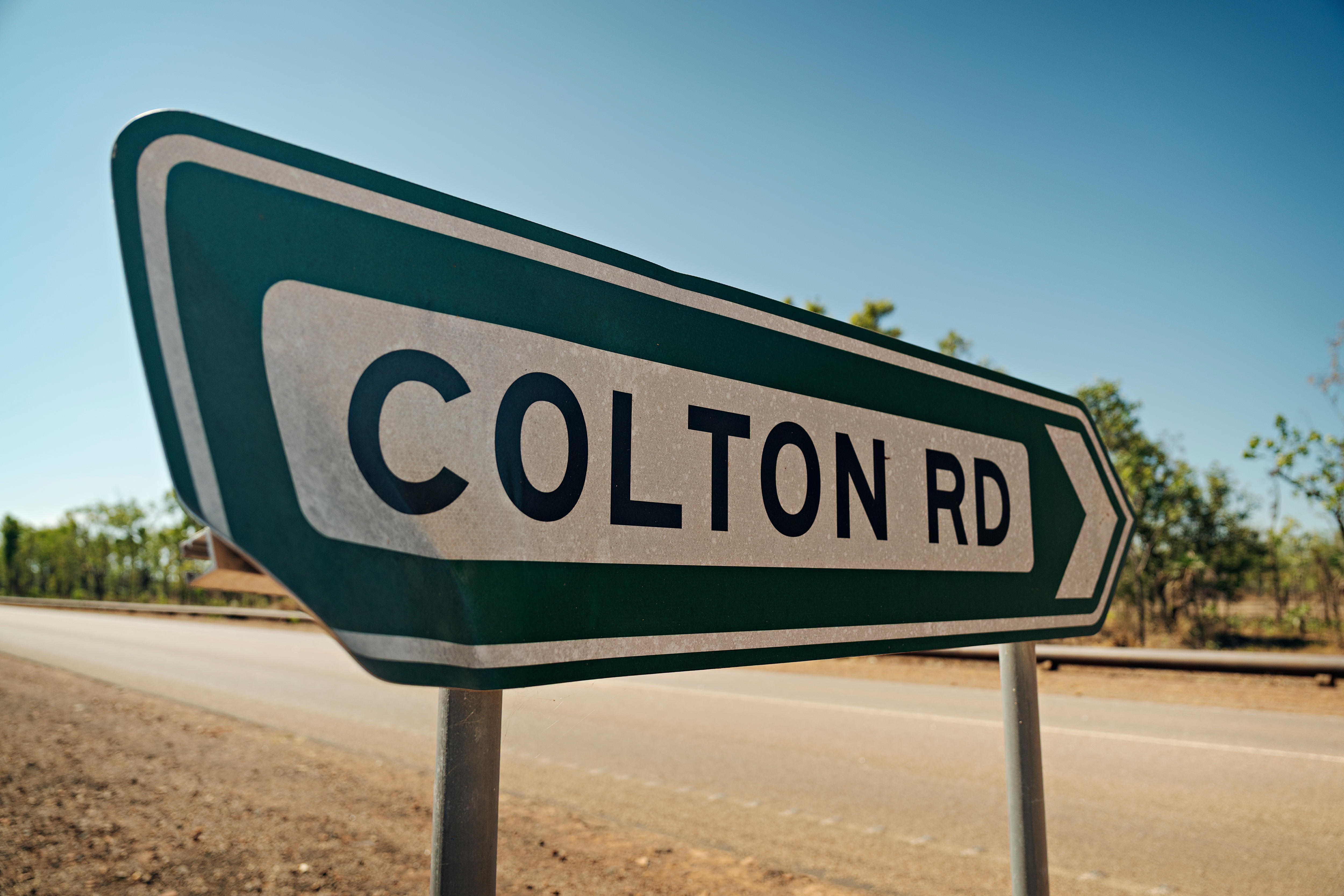 An aged street sign reads Colton Road in a bush backdrop.
