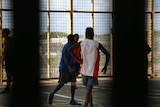 Inmates at Don Dale play basketball on a court enclosed by bars and fencing.