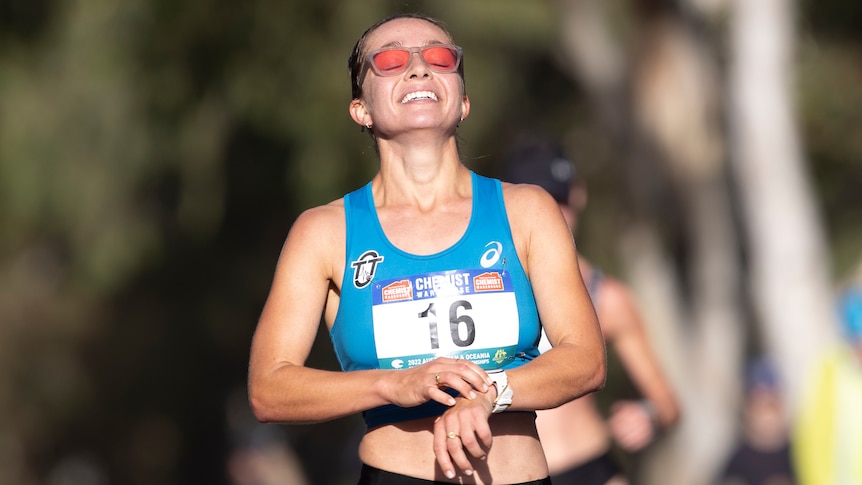 A woman athlete stops her watch and grins after winning an event
