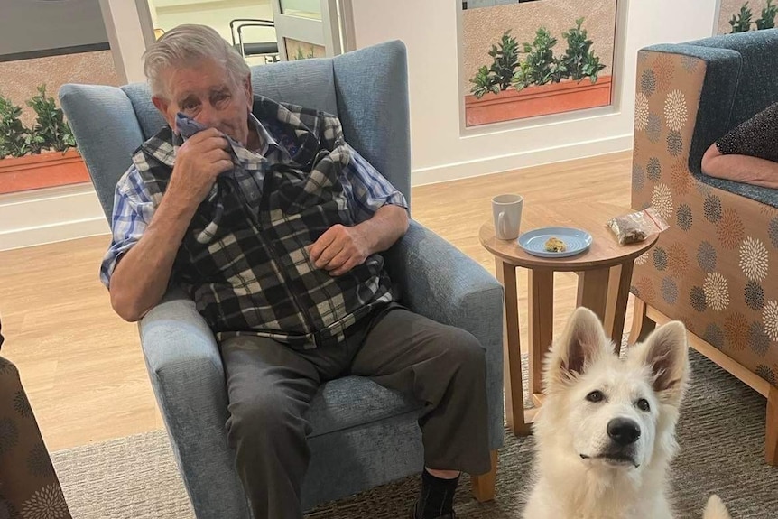 An elderly man sitting down with a white dog next to him.